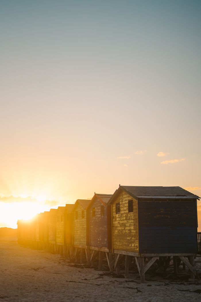 Breathtaking sunset view over wooden beach huts in Cape Peninsula, capturing nature's golden hour glow.